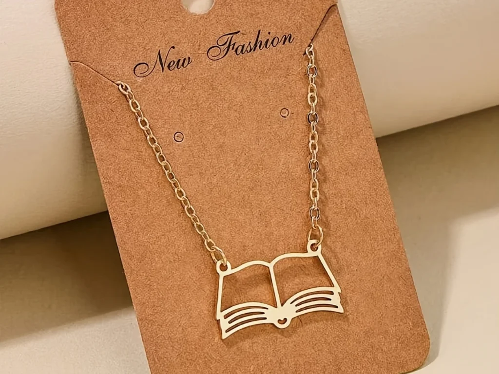 Gold-tone open book pendant necklace displayed on card