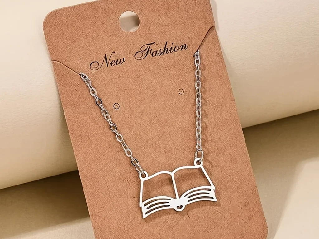 Silver-tone open book pendant necklace displayed on card