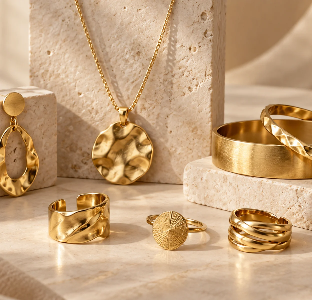 Custom brass earrings, necklace, bracelets and rings displayed on warm neutral stone