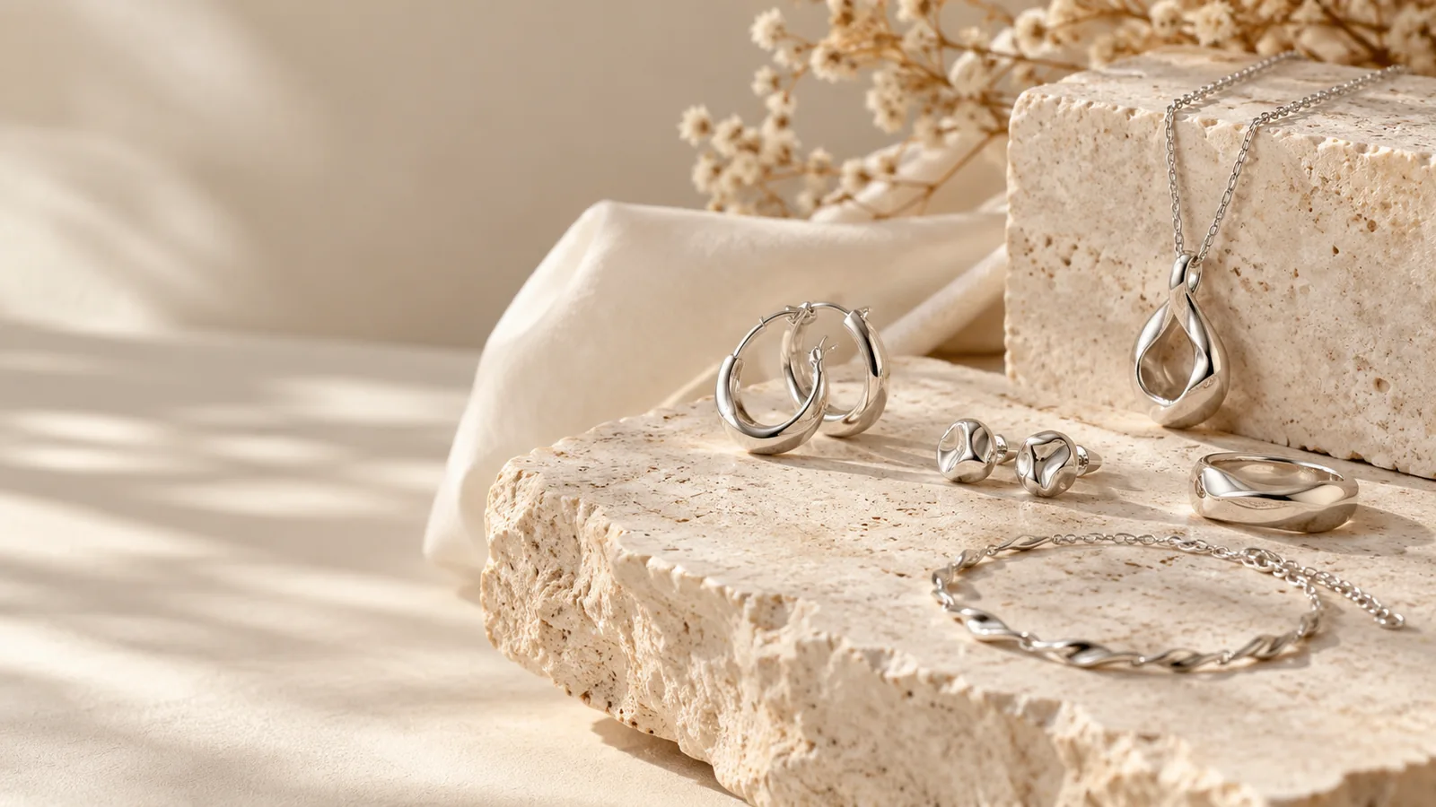 Custom sterling silver jewelry design concept with necklace, ring, earrings and bracelet arranged on warm stone
