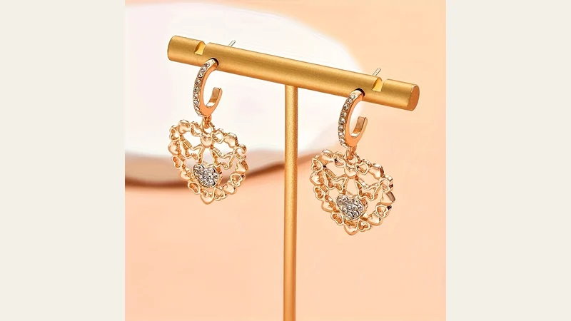 Heart-shaped gold-tone hoop earrings displayed on a horizontal stand